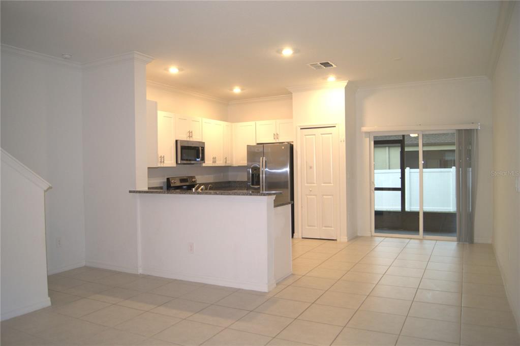 A kitchen with white cabinets, stainless steel appliances, and a breakfast bar overlooks a tiled area — 36347 CAMP FIRE TERRACE, ZEPHYRHILLS, FL