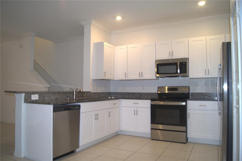 A kitchen features white cabinets, stainless steel appliances, and granite countertops with a tile floor — 36347 CAMP FIRE TERRACE, ZEPHYRHILLS, FL