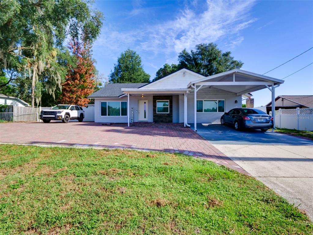 A single-story house with a brick driveway, attached carport, and two parked cars — 1915 E LAKE DRIVE, CASSELBERRY, FL
