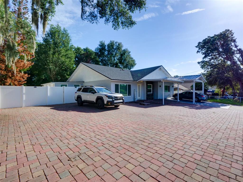 A single-story house with a large brick-paved driveway, a white fence, and a carport — 1915 E LAKE DRIVE, CASSELBERRY, FL