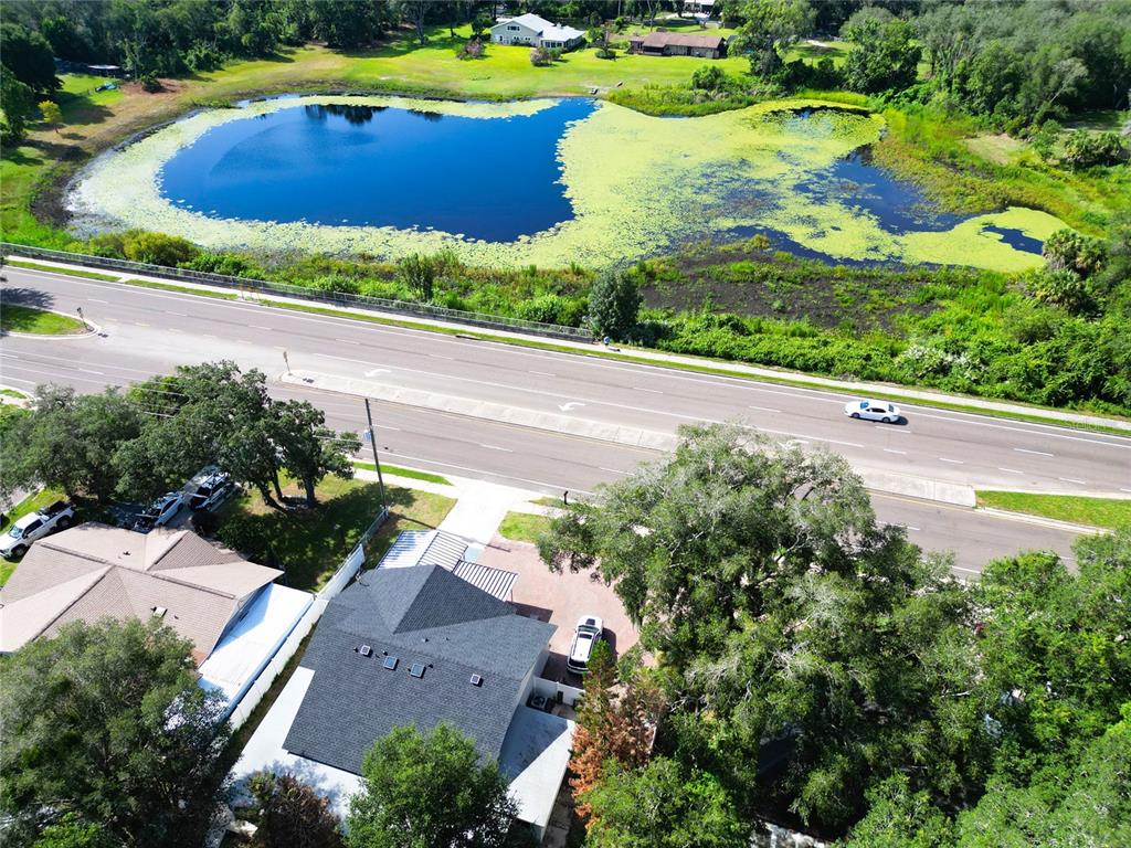 An aerial view shows a house with a dark roof next to a road and pond — 1915 E LAKE DRIVE, CASSELBERRY, FL