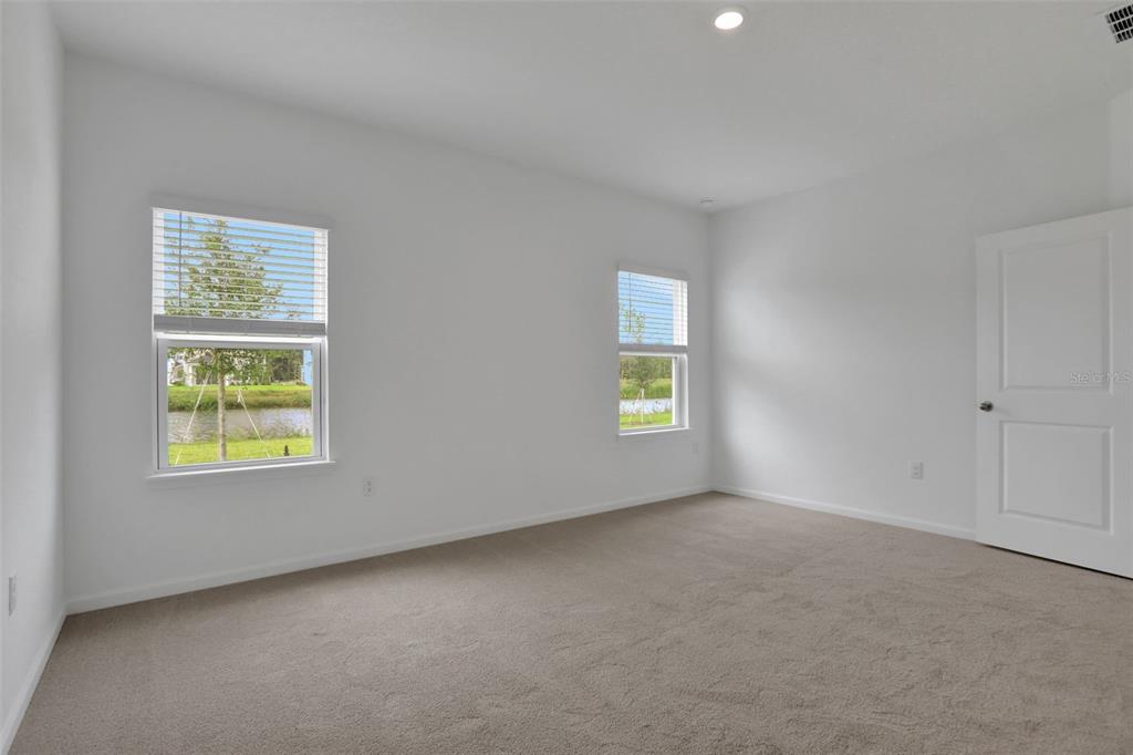 An empty bedroom with white walls, beige carpet, two windows, and a white door — 204 DONOVAN DRIVE, ST AUGUSTINE, FL