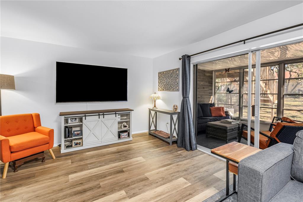 A living room features wood-look flooring, a wall-mounted television, and sliding glass doors to a patio — 3620 41ST WAY S UNIT F, ST PETERSBURG, FL