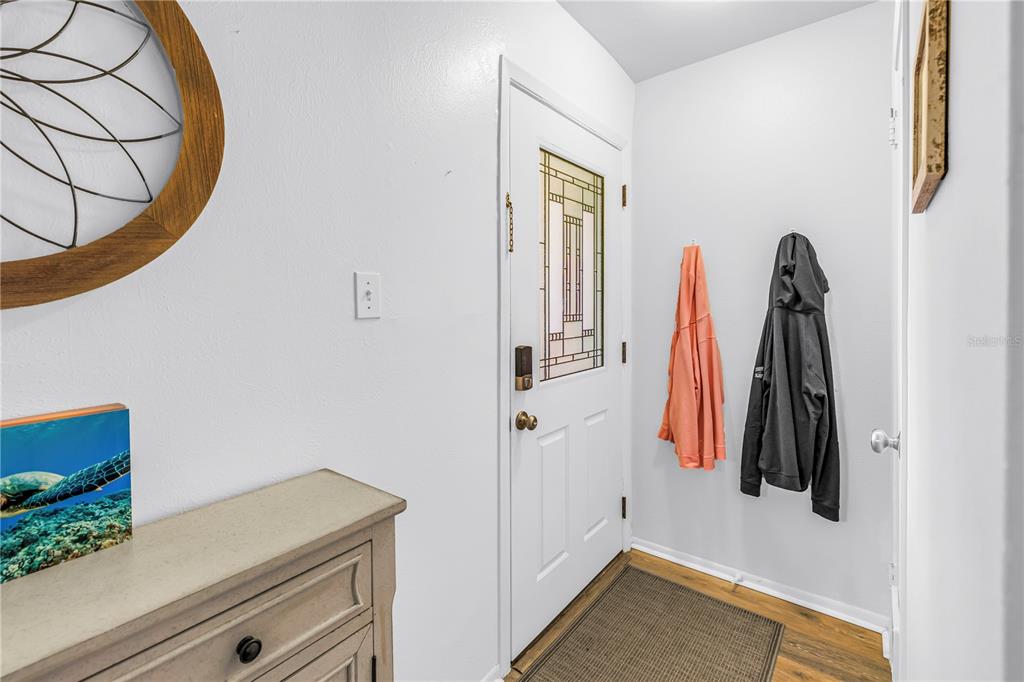 An entryway features a white door with a glass insert, a wood dresser, and wall hooks — 3620 41ST WAY S UNIT F, ST PETERSBURG, FL