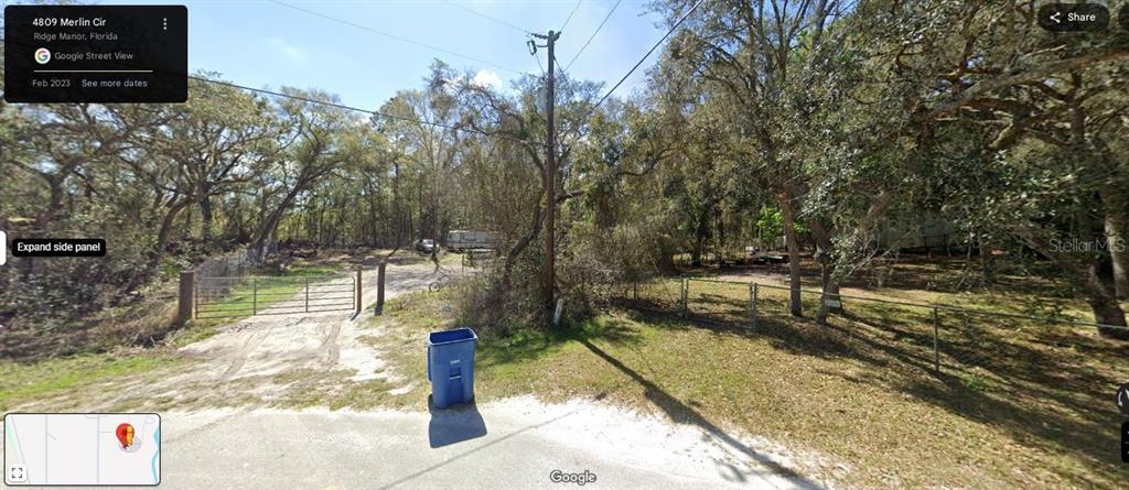 A gated dirt driveway leads into a wooded lot with a blue trash bin nearby — 4809 MERLIN CIRCLE, RIDGE MANOR, FL