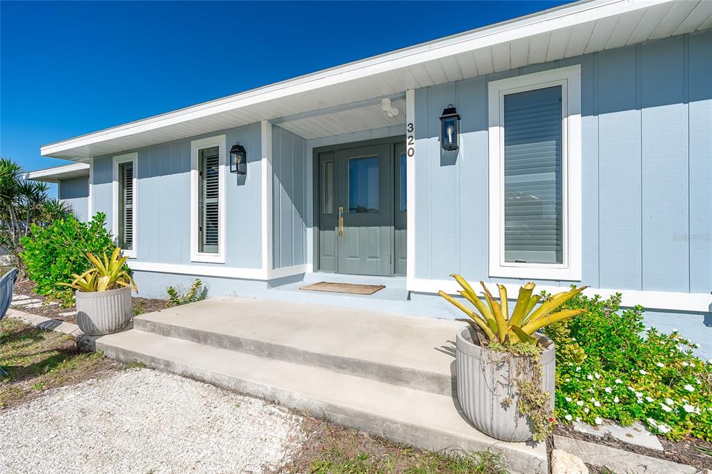 A light blue house exterior features a gray front door, concrete steps, and potted plants — 320 ANCHOR ROW, PLACIDA, FL