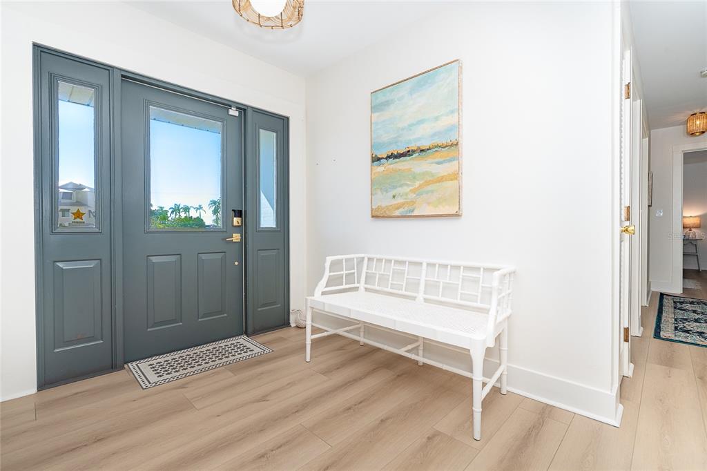 An entryway features light wood flooring, a white bench, and a dark gray front door — 320 ANCHOR ROW, PLACIDA, FL