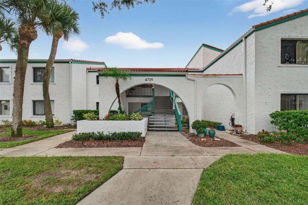 A two-story white stucco apartment building features a central arched entryway and exterior stairs — 4729 CASABLANCA UNIT C25, SEBRING, FL