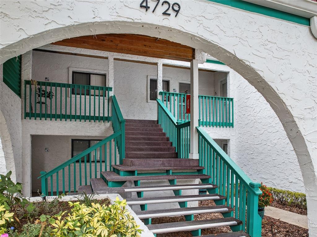 An exterior view of a multi-story building entrance featuring teal railings and concrete stairs — 4729 CASABLANCA UNIT C25, SEBRING, FL