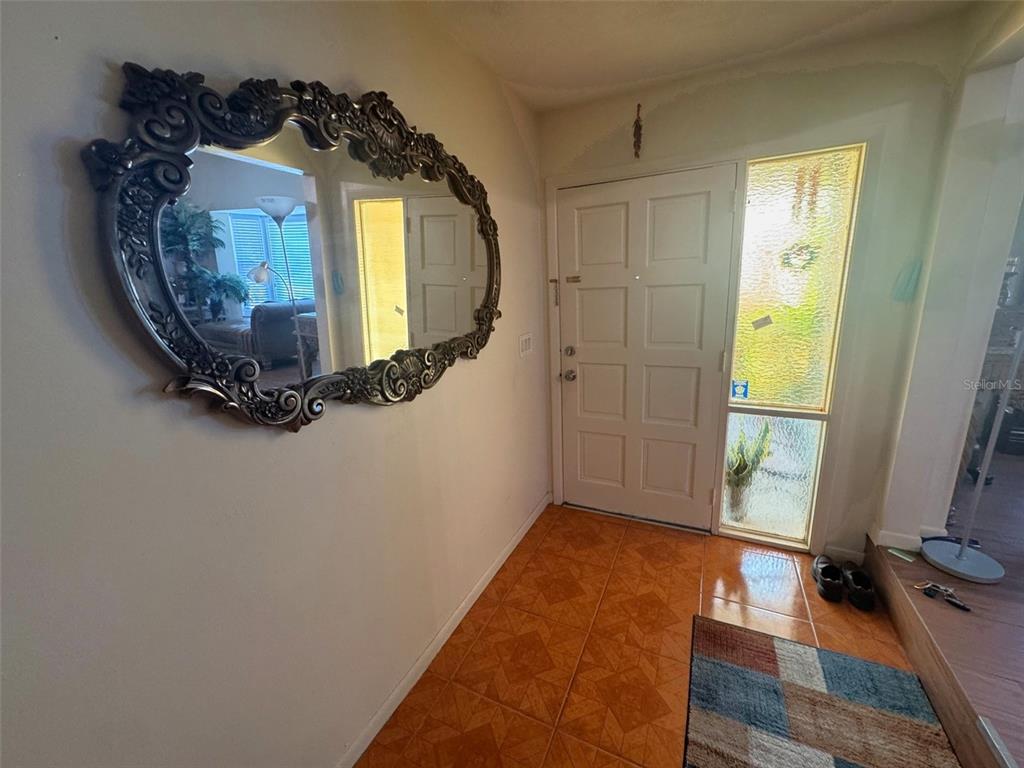 An entryway features a large ornate mirror on a wall, tiled flooring, and a front door — 3146 CARLOS DRIVE, DUNEDIN, FL