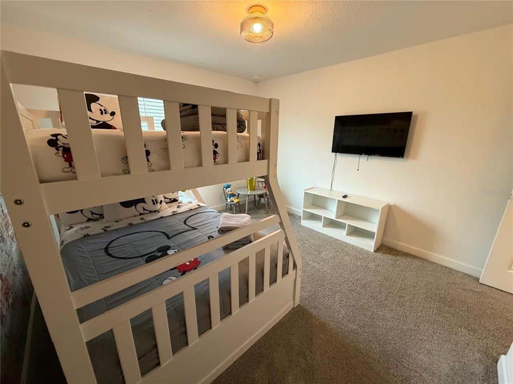 A bedroom features a white bunk bed with Mickey Mouse bedding, a wall-mounted television, and carpet — 2669 READING TRAIL, KISSIMMEE, FL