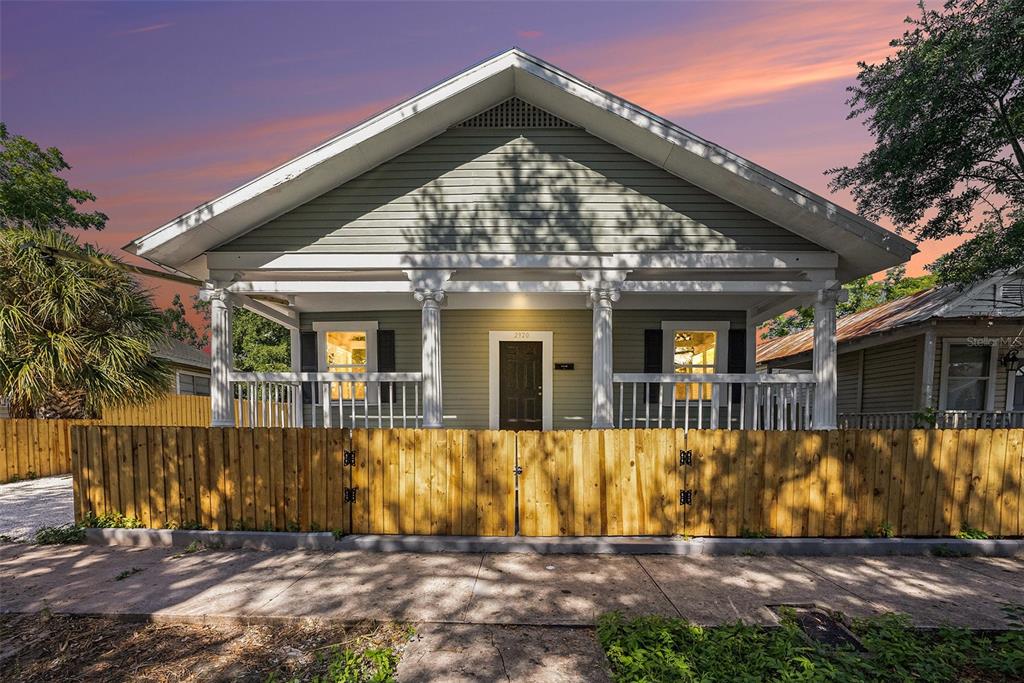 A light green bungalow with a front porch and wooden fence at sunset — 2920 N 17TH STREET, TAMPA, FL
