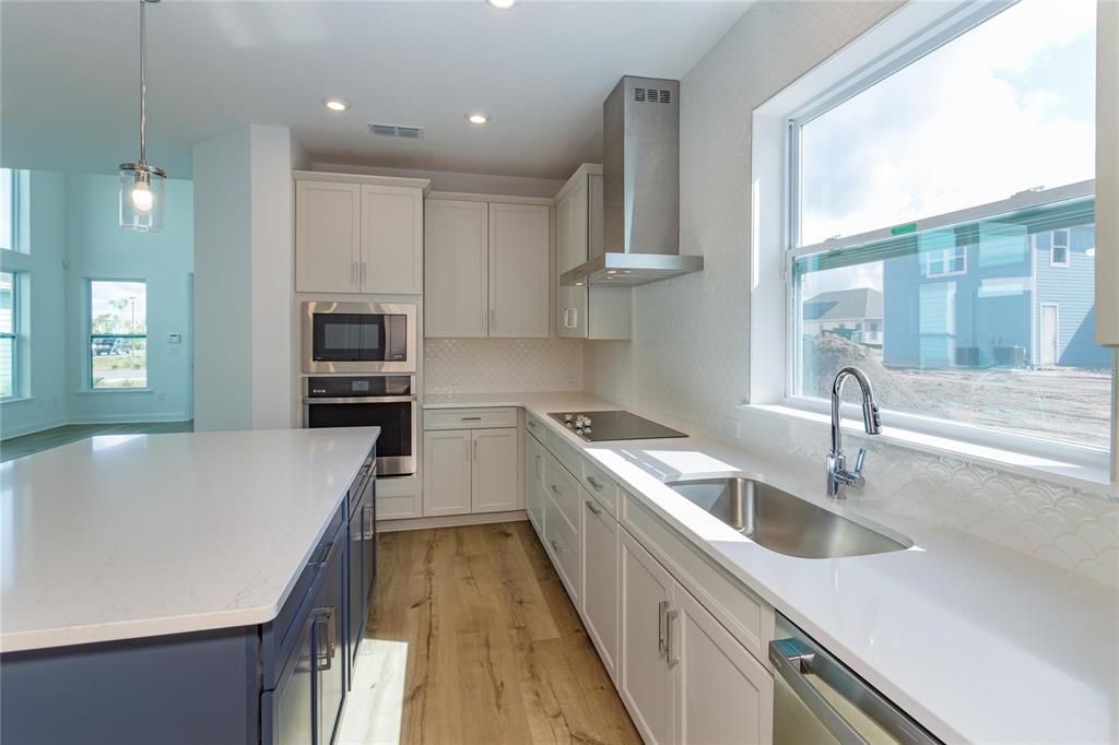 A modern kitchen features white cabinets, a blue island, stainless steel appliances, and wood flooring — 6521 ROVER WAY, ST CLOUD, FL