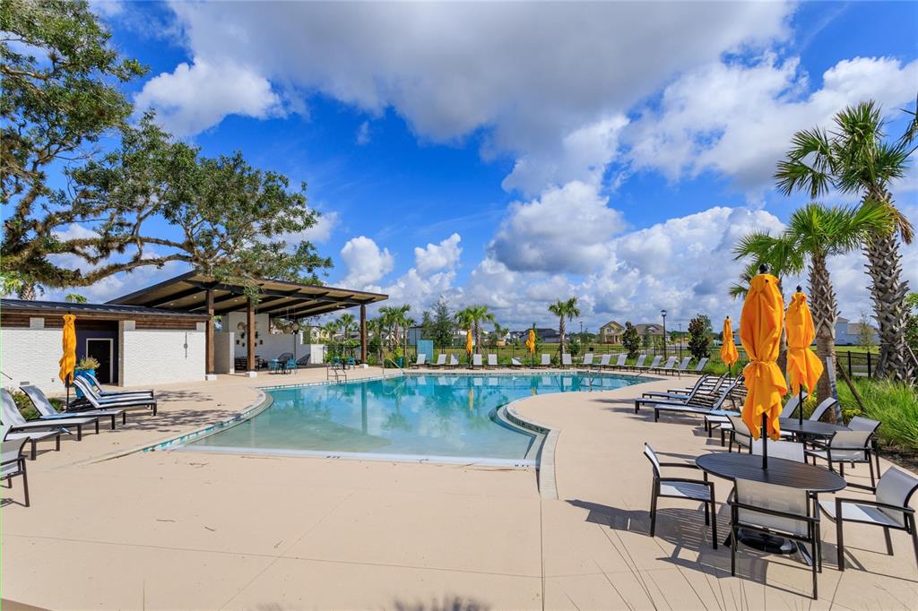 A swimming pool with lounge chairs and umbrellas sits in front of a covered patio area — 6521 ROVER WAY, ST CLOUD, FL