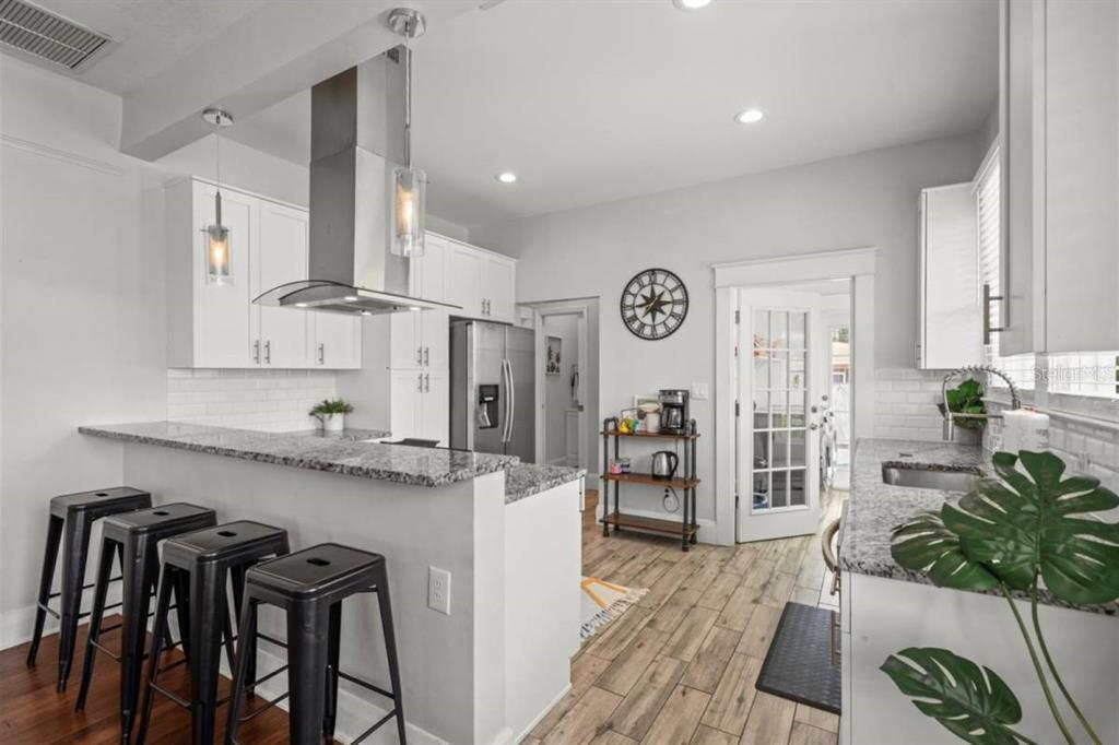 A kitchen features white cabinets, stainless steel appliances, granite countertops, and a sun-patterned area rug — 7002 N CAMERON AVENUE, TAMPA, FL