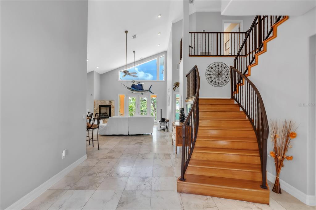 A foyer with light tile flooring features a curved wooden staircase and a vaulted ceiling — 1508 BOWLEES COVE, BRADENTON, FL