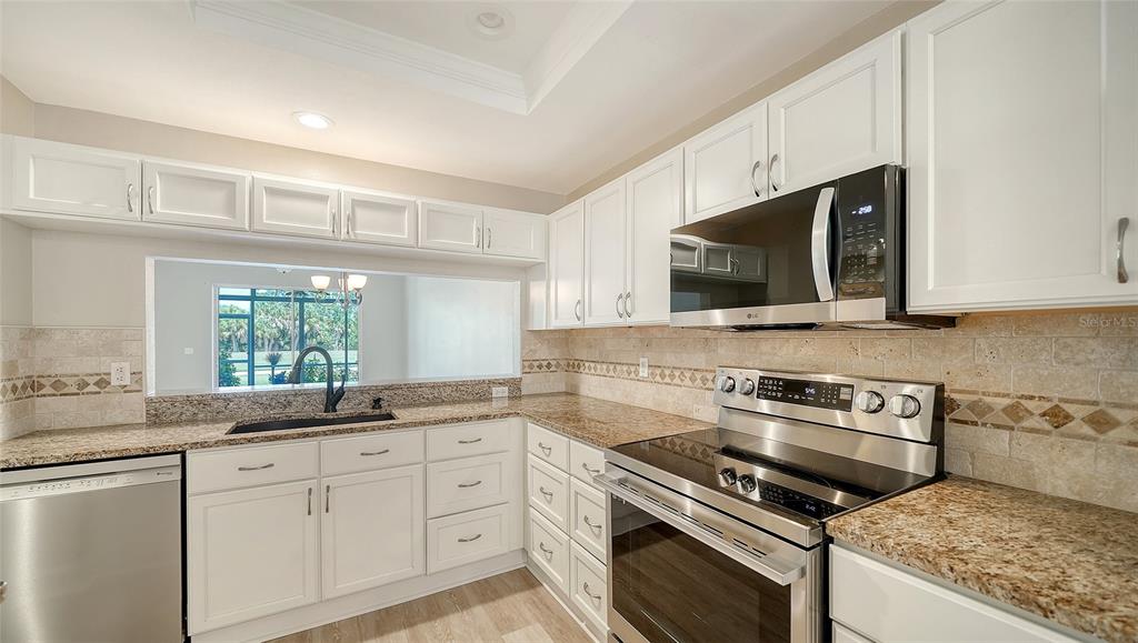 A kitchen with white cabinets, granite countertops, stainless steel appliances, and a pass-through window — 8735 OLDE HICKORY AVENUE UNIT 8105, SARASOTA, FL