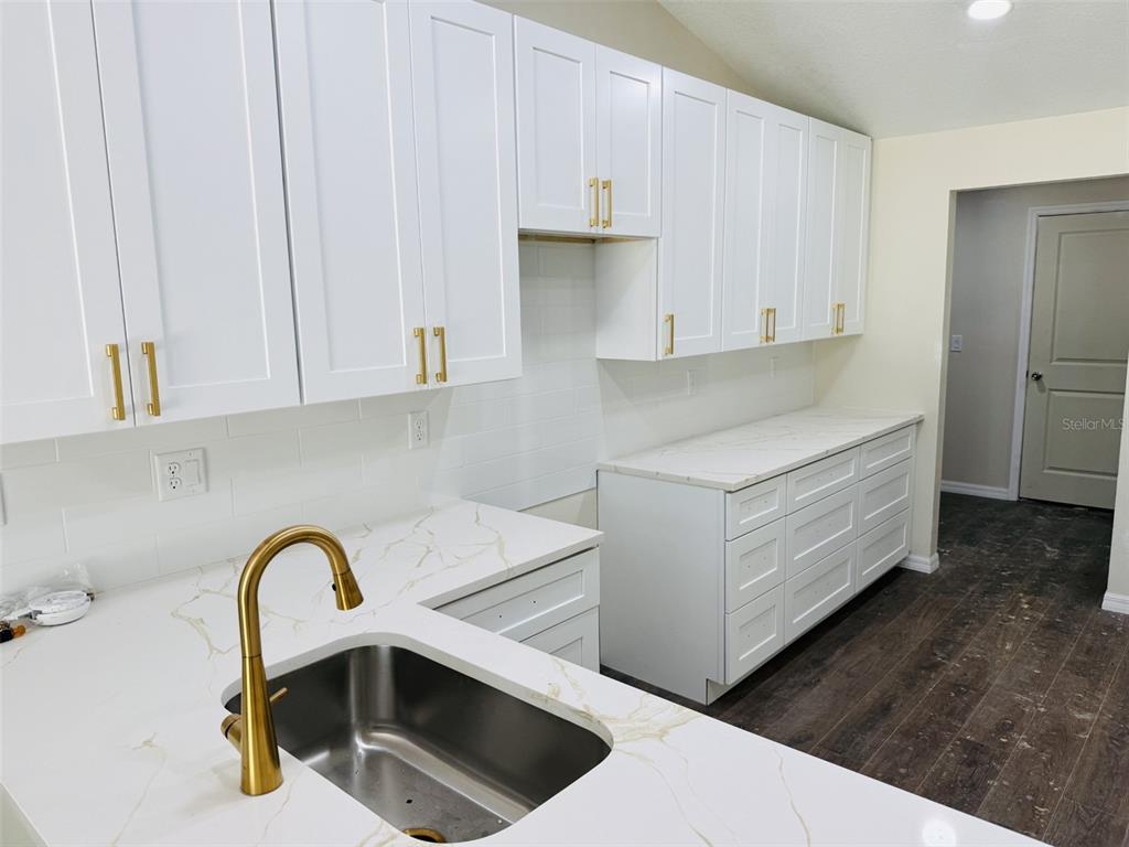 A kitchen features white shaker cabinets, gold hardware, and white marble-look countertops with a sink — 13475 CANYON SWALLOW ROAD, WEEKI WACHEE, FL