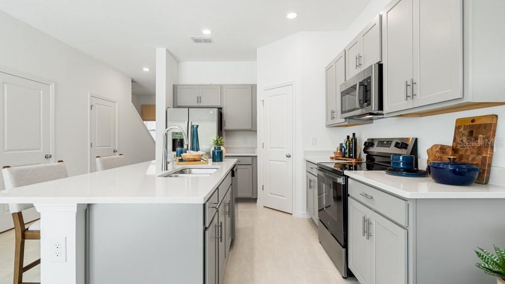 A modern kitchen features gray cabinets, a white island with bar stools, and an adjacent living area — 7117 PINELIT COVE, NOKOMIS, FL