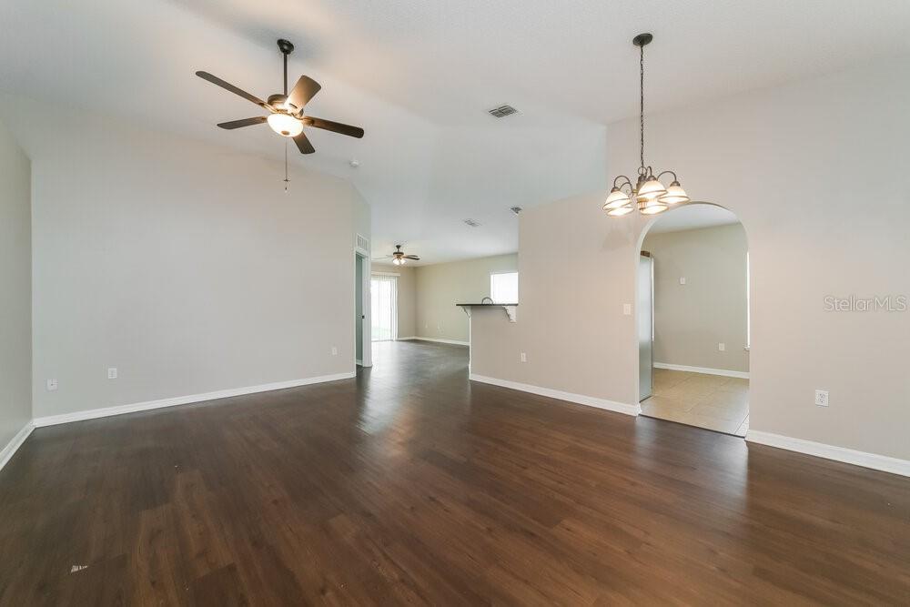 An open-concept living area features dark wood-look flooring, a ceiling fan, and a dining chandelier — 5470 SILVER THISTLE LANE, ST CLOUD, FL