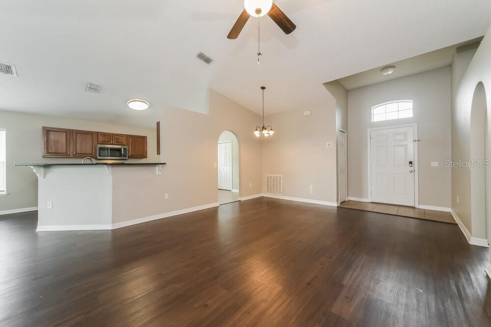 An open-concept living and dining area features dark wood flooring, vaulted ceilings, and a kitchen — 5470 SILVER THISTLE LANE, ST CLOUD, FL