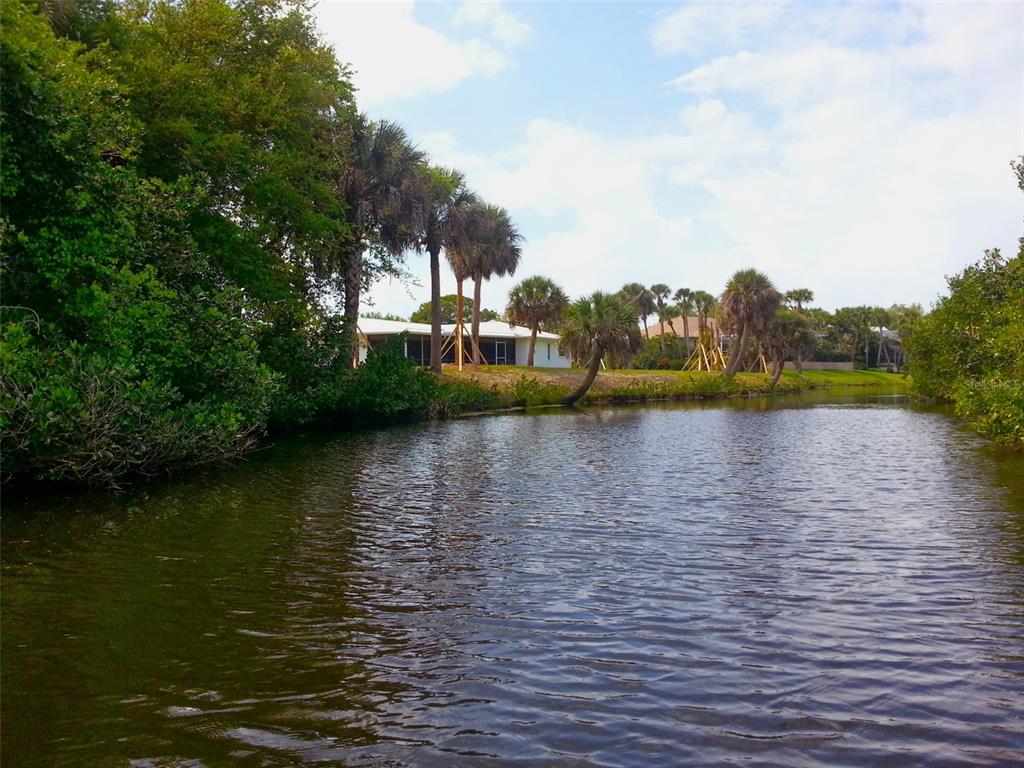 A view of a canal lined with trees and palm trees leading toward a house — 120 BARRACUDA DRIVE, PLACIDA, FL