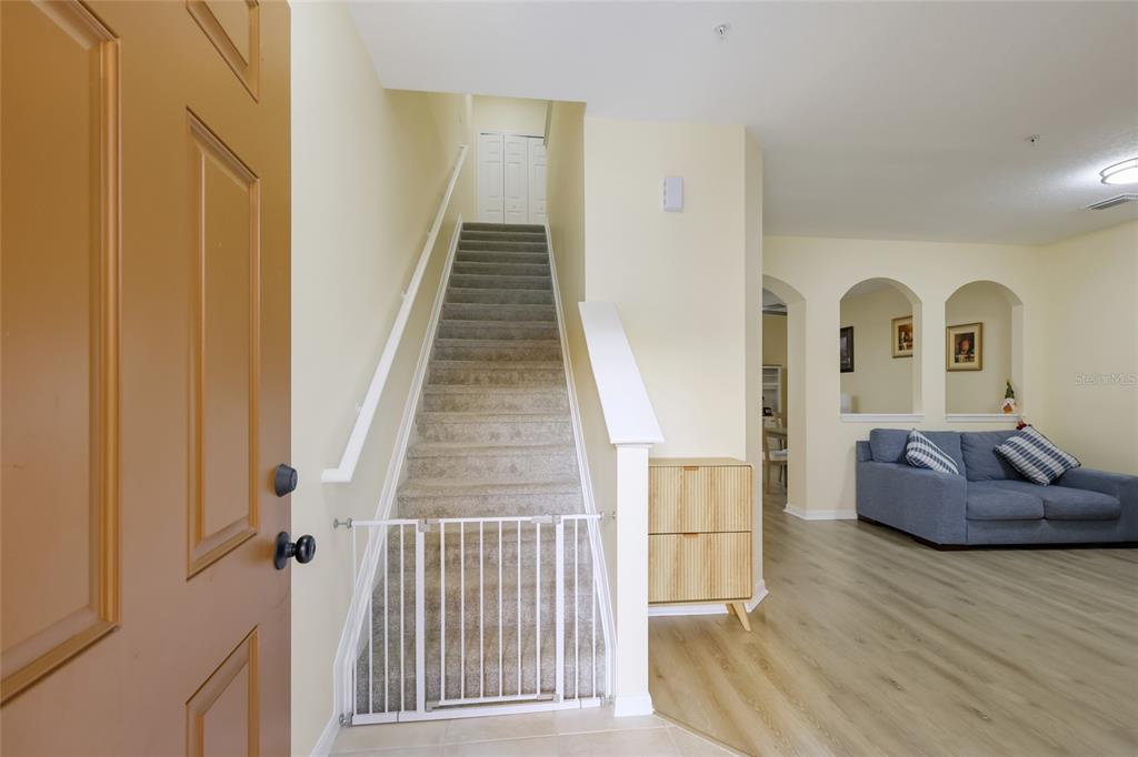 An entryway features a carpeted staircase with a safety gate, light wood flooring, and a living area — 3793 PARKRIDGE CIRCLE UNIT 3-105, SARASOTA, FL