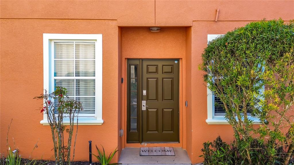A front entrance with an orange stucco exterior, a dark door, and a small bush — 885 ASSEMBLY COURT, REUNION, FL