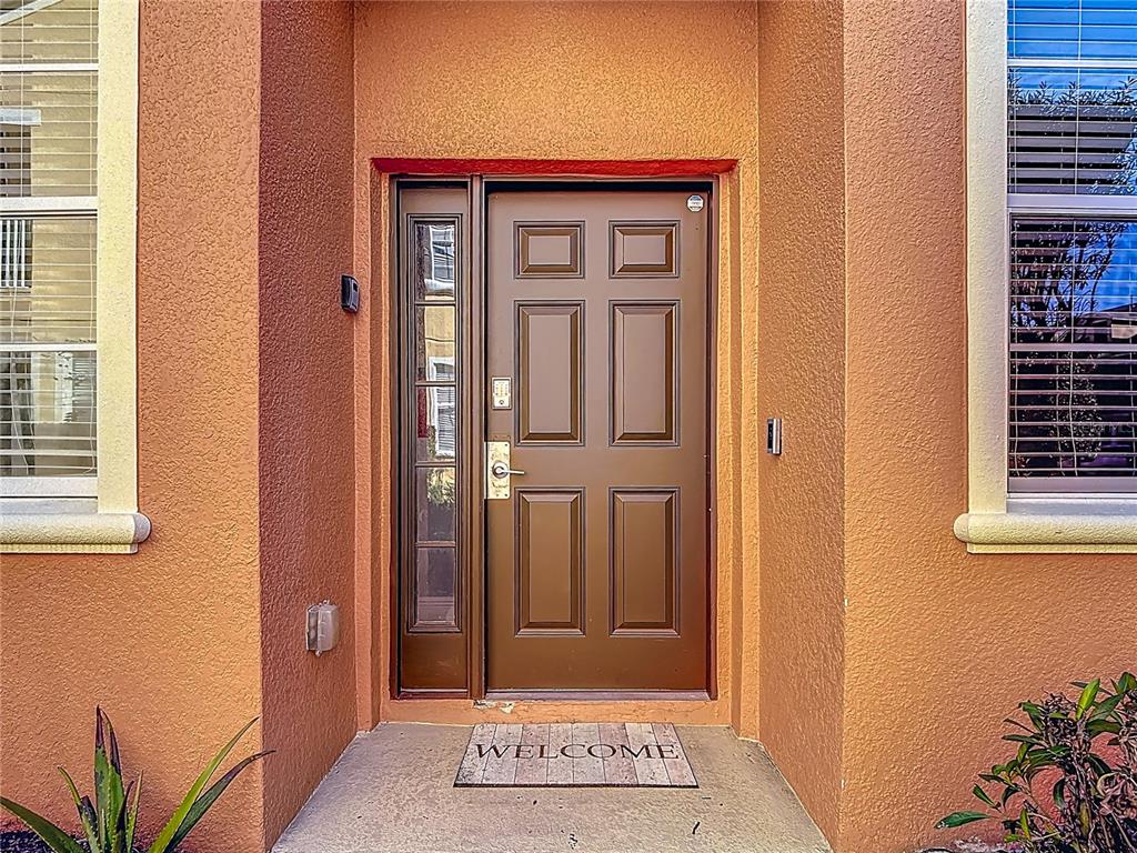 A brown front door with a side window sits in an orange stucco entryway — 885 ASSEMBLY COURT, REUNION, FL