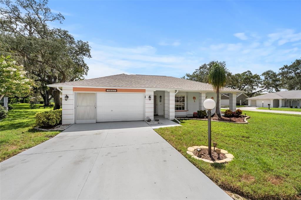 A single-story house with a white garage, concrete driveway, and a front lawn with trees — 8643 GOLD PINE DRIVE, PORT RICHEY, FL