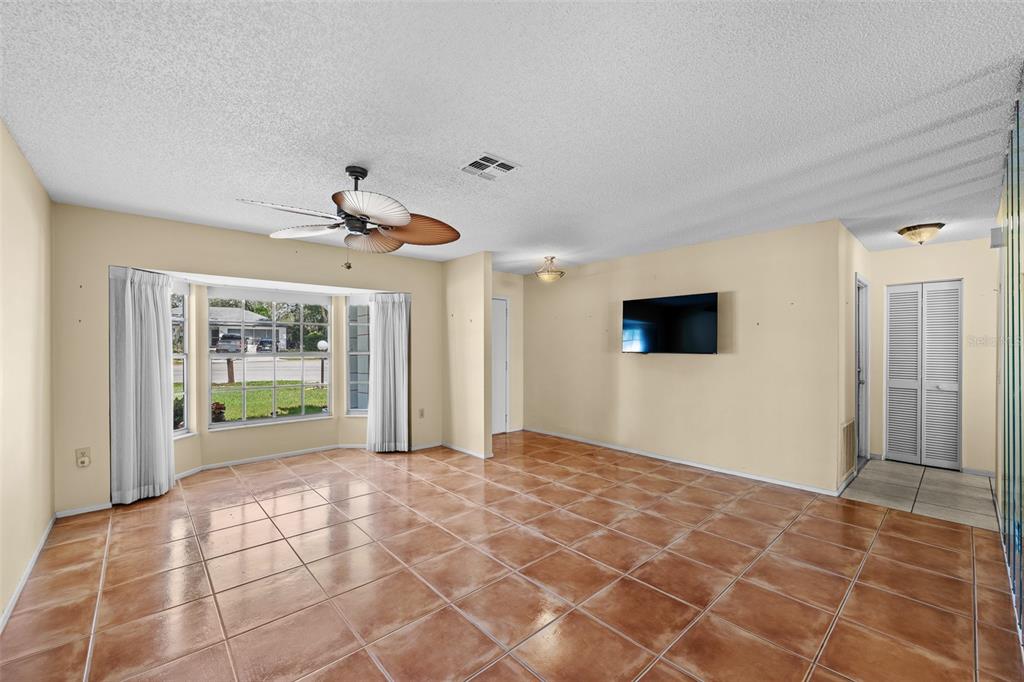 A living room with beige walls, brown tile flooring, a ceiling fan, and a bay window — 8643 GOLD PINE DRIVE, PORT RICHEY, FL