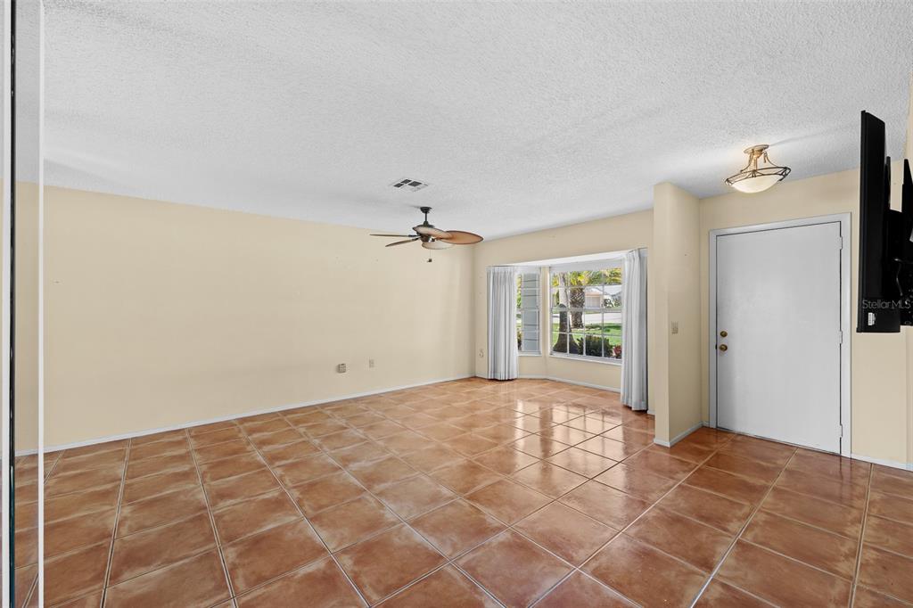 An empty living room features light-colored walls, brown tile flooring, a ceiling fan, and windows — 8643 GOLD PINE DRIVE, PORT RICHEY, FL