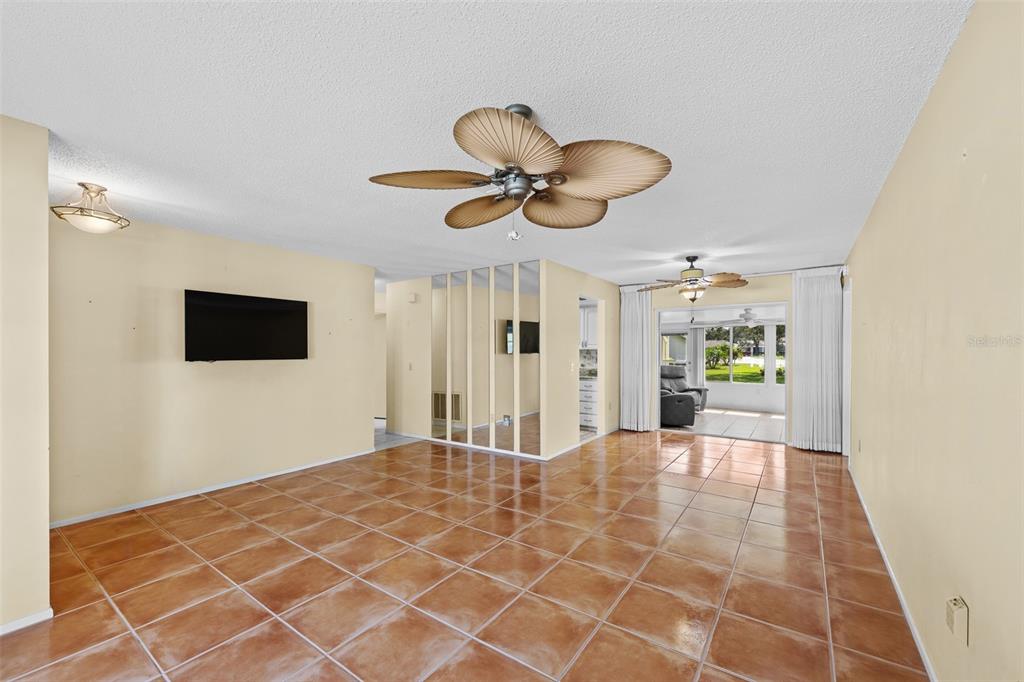 A living room with tan tile flooring, a ceiling fan, and a mirrored wall divider — 8643 GOLD PINE DRIVE, PORT RICHEY, FL