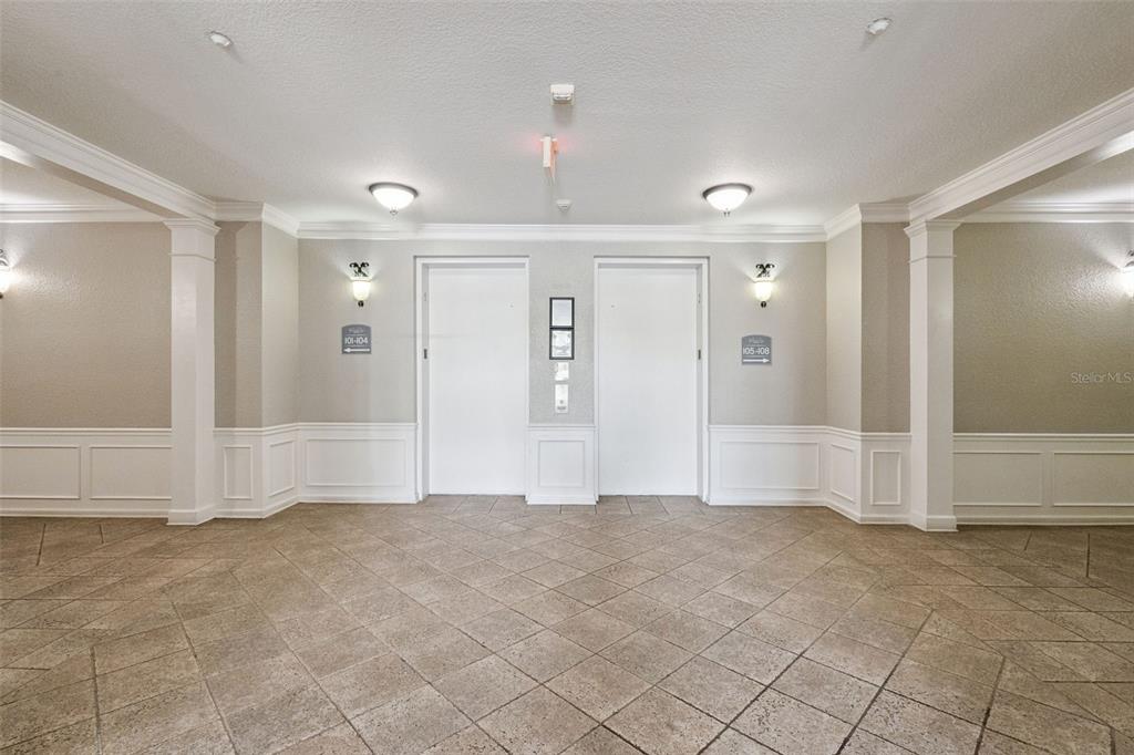 A tiled elevator lobby features two white doors, wall sconces, and directional signage — 4840 CAYVIEW AVENUE UNIT 405, ORLANDO, FL