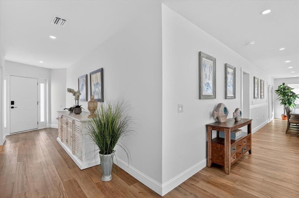 A bright entryway and hallway feature light wood floors, white walls, and decorative console tables — 2201 WEBBER STREET, SARASOTA, FL