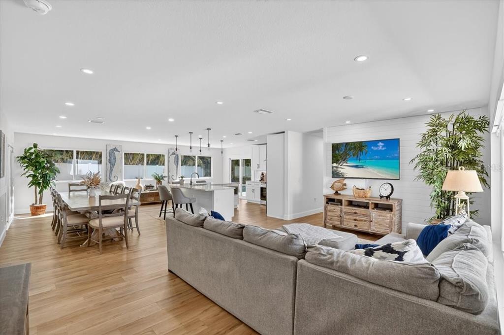 An open-concept living room and kitchen featuring light wood floors, white walls, and coastal decor — 2201 WEBBER STREET, SARASOTA, FL