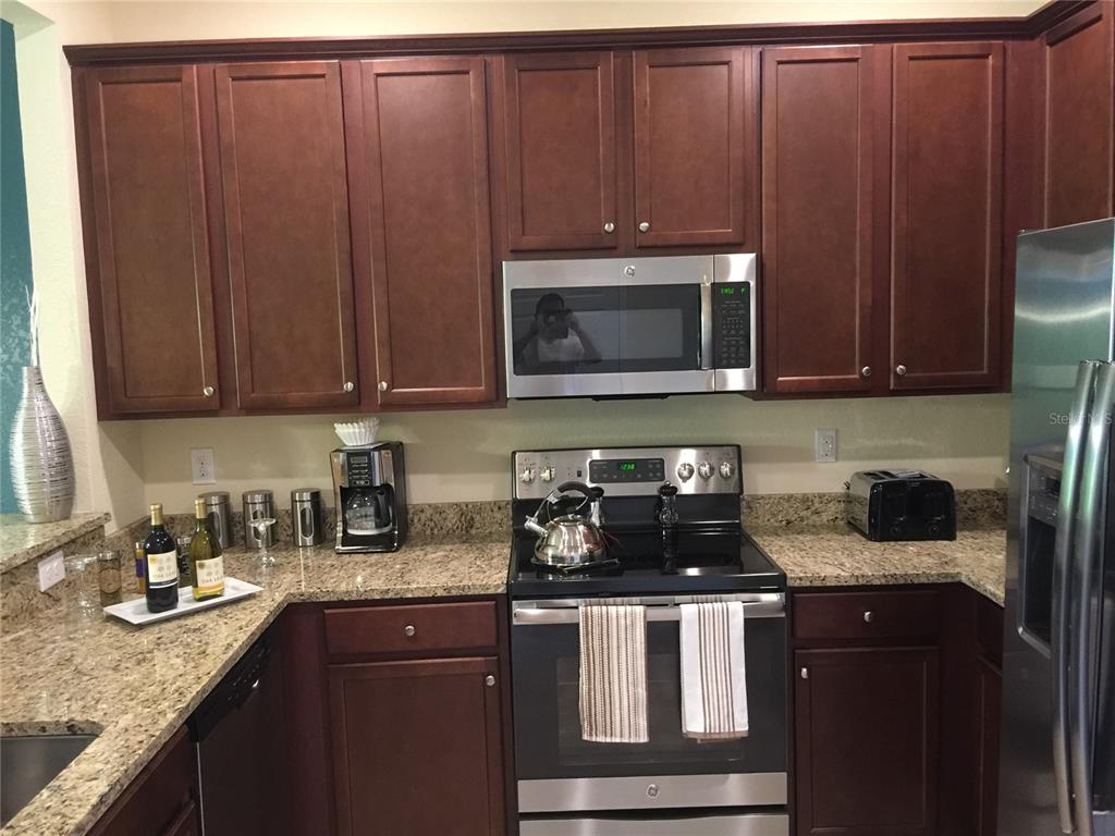 A kitchen features dark wood cabinets, granite countertops, stainless steel appliances, and a microwave oven — 7216 KETCH PLACE, BRADENTON, FL