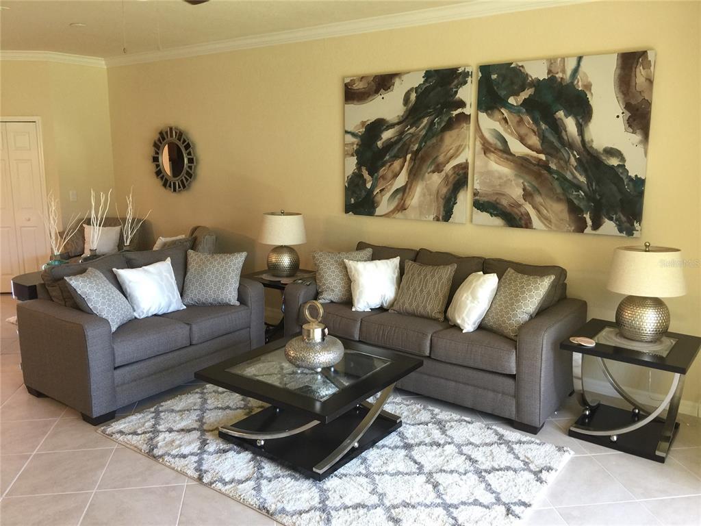A living room features a grey sofa and loveseat, a coffee table, and abstract wall art — 7216 KETCH PLACE, BRADENTON, FL