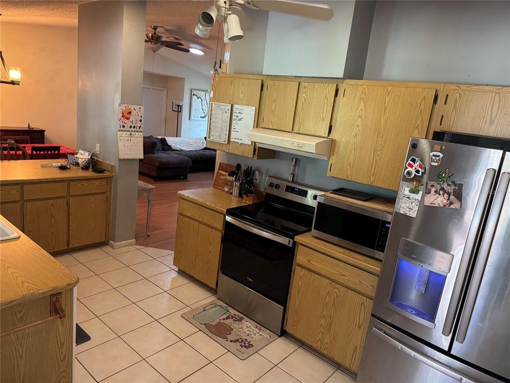 A kitchen features oak cabinets, stainless steel appliances, and tiled flooring, opening into a living room — 5 BANNER LANE, PALM COAST, FL