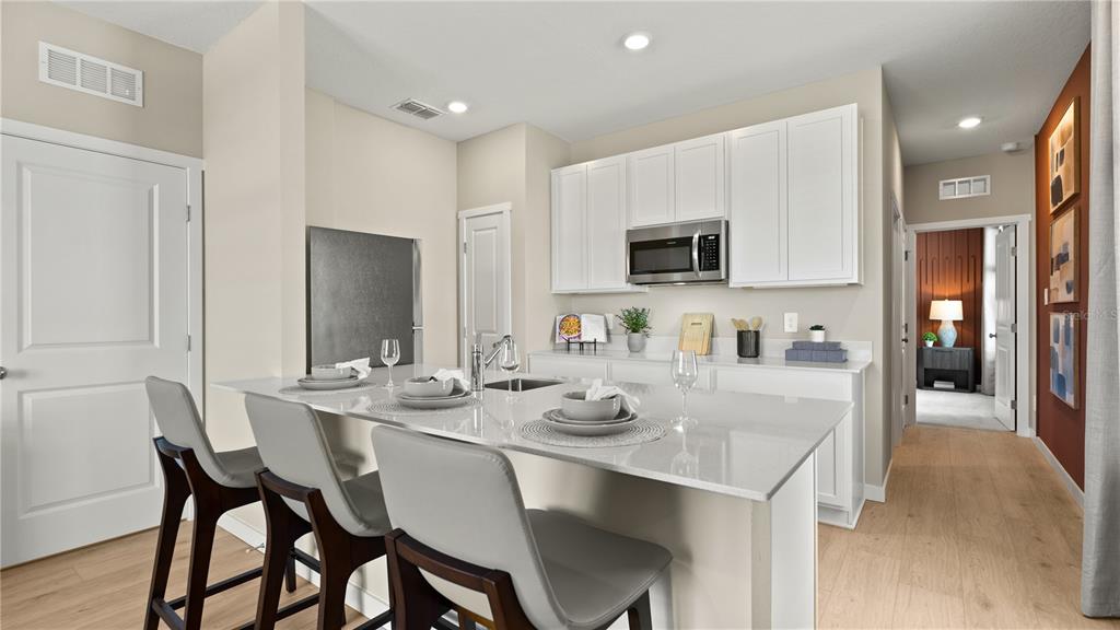 A modern kitchen features white cabinetry, a quartz island with bar seating, and light flooring — 167 GLENFIELD DRIVE, DAVENPORT, FL