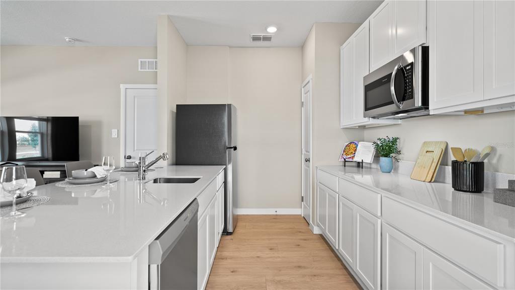 A modern kitchen features white cabinets, quartz countertops, stainless steel appliances, and light wood flooring — 167 GLENFIELD DRIVE, DAVENPORT, FL