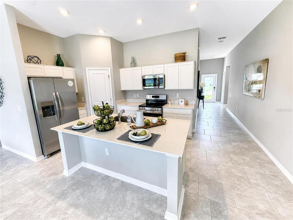 A kitchen features white cabinets, stainless steel appliances, a central island, and light tile flooring — 1104 TYLER LOOP, WINTER HAVEN, FL
