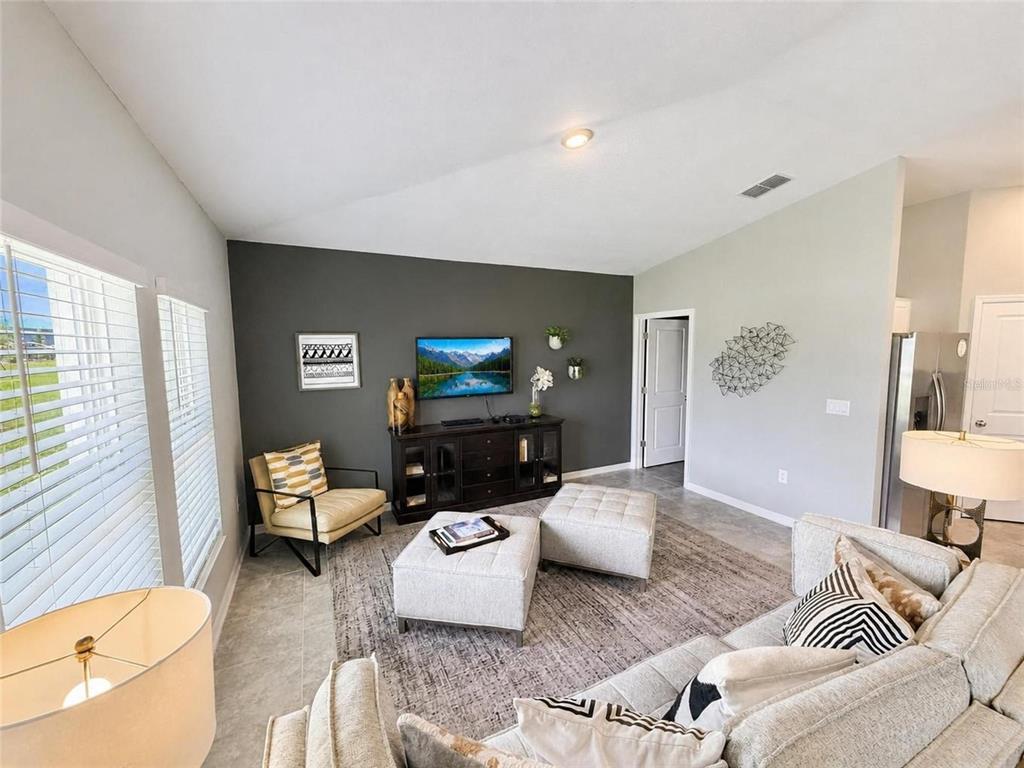 A living room features a dark accent wall, a television, two ottomans, and neutral furniture — 1104 TYLER LOOP, WINTER HAVEN, FL