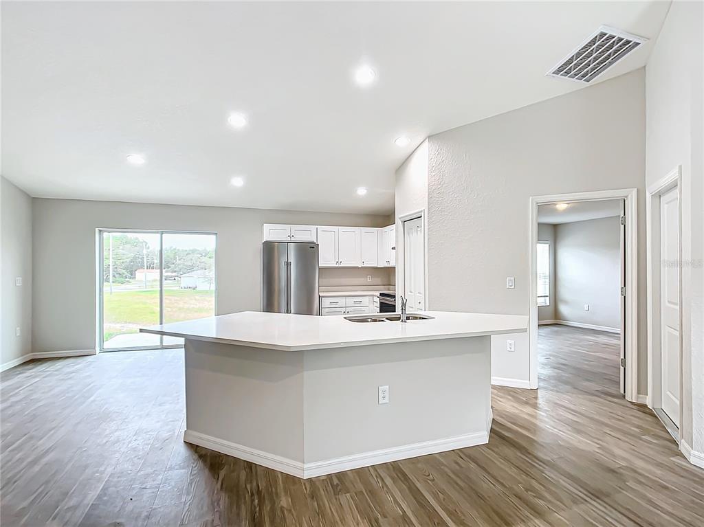 A kitchen with a white island, stainless steel refrigerator, and light wood-look flooring — 12063 SE 89TH AVENUE, BELLEVIEW, FL