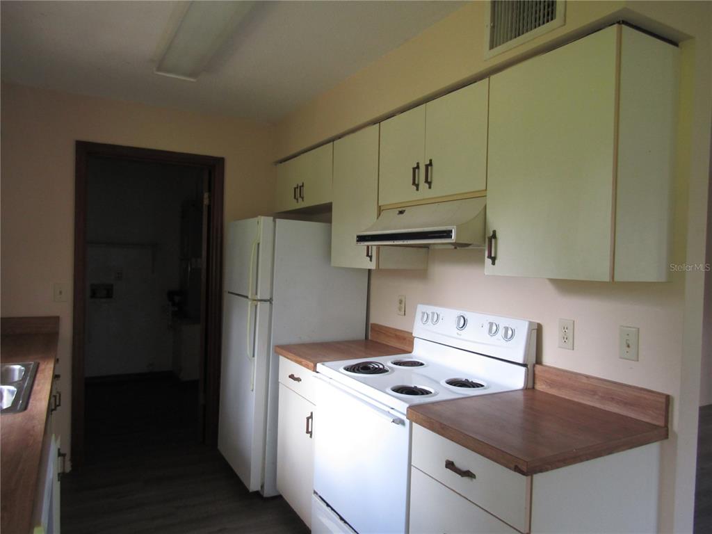 A kitchen features white cabinets, a white stove, a white refrigerator, and wood-look countertops — 993 FOOTE STREET, EUSTIS, FL