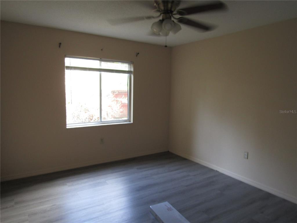 An empty bedroom features light-colored walls, gray wood-look flooring, a ceiling fan, and a window — 993 FOOTE STREET, EUSTIS, FL