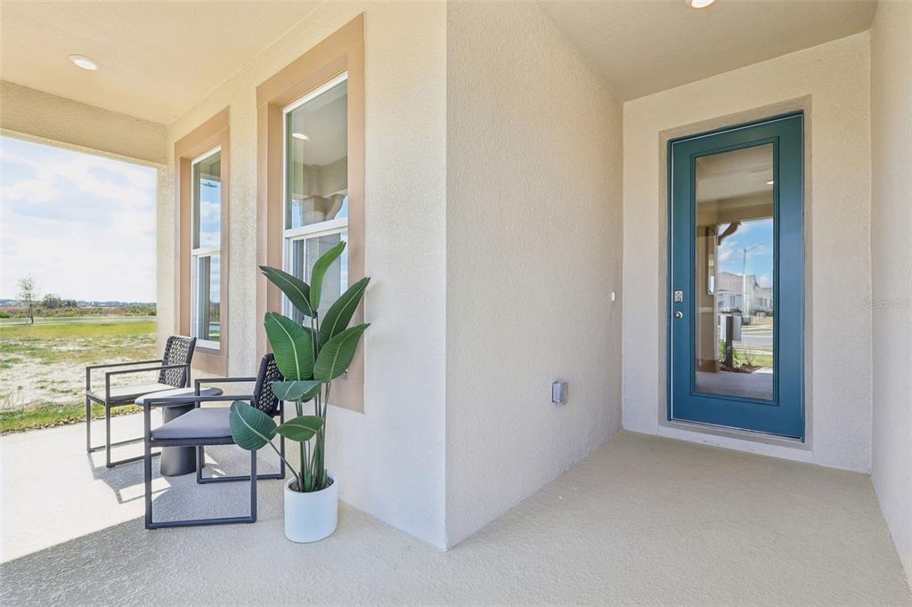 A covered porch features a blue glass-paneled door, two outdoor chairs, and a potted plant — 8595 HEMPSTEAD WAY, MOUNT DORA, FL