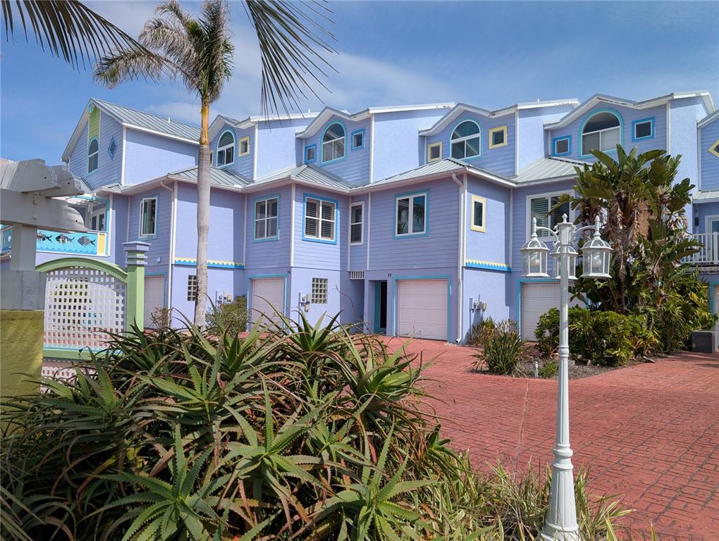 A multi-story lavender townhouse complex features white garage doors and a red brick driveway — 3000 OCEAN SHORE BOULEVARD UNIT 14, ORMOND BEACH, FL