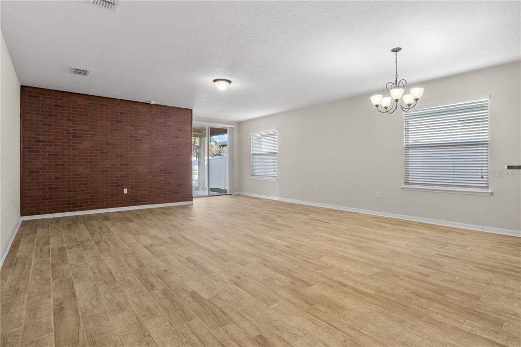 A spacious living room features light wood-look flooring, a red brick accent wall, and chandelier lighting — 8017 PAGE COURT, HAINES CITY, FL