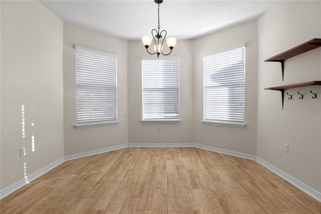 An empty dining area features light wood-look flooring, three windows with blinds, and a chandelier — 8017 PAGE COURT, HAINES CITY, FL